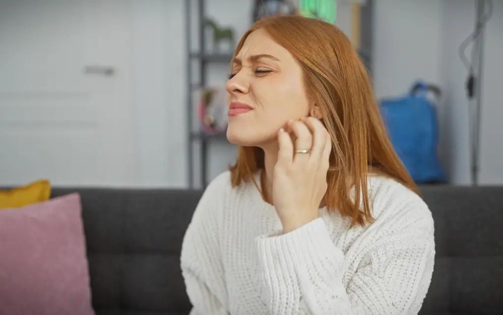 Kobieta ze skrzywioną miną drapie się palcami po swędzącej skórze twarzy