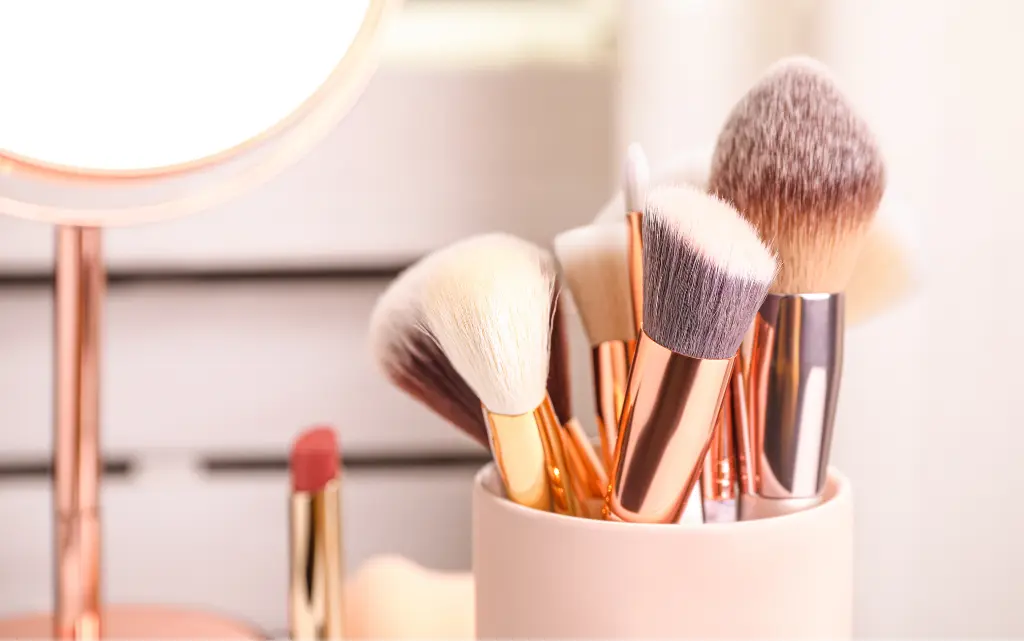 Pędzle do makijażu w beżowym pojemniku, w tle lusterko kosmetyczne