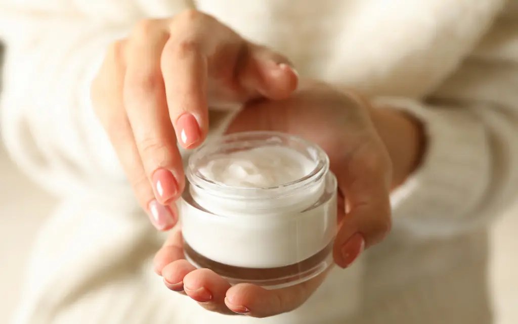 Kobiece dłonie trzymają słoiczek z kremem do twarzy