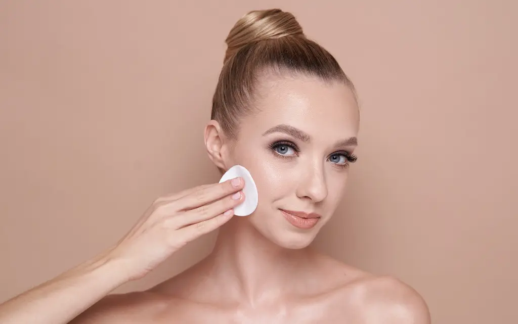 Młoda kobieta wykonuje demakijaż płatkiem kosmetycznym