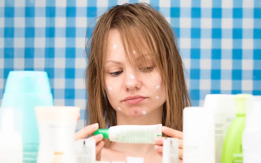 Kobieta z mokrymi włosami w łazience czyta skład kremu do twarzy