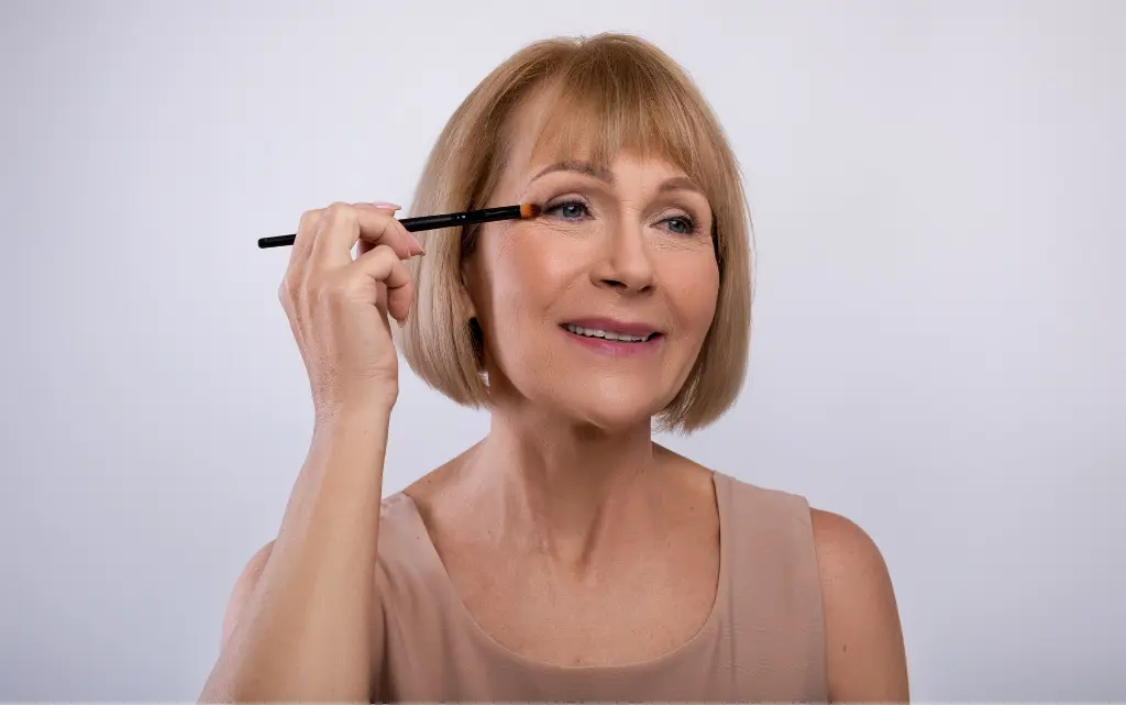 Starsza kobieta wykonuje makijaż oka smokey eye