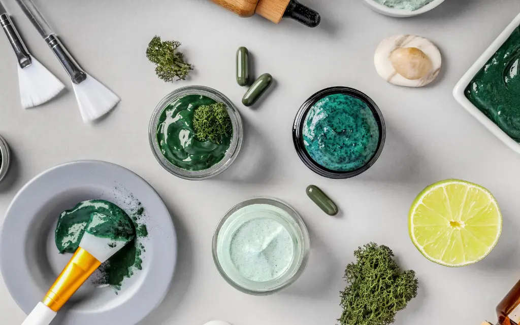 Różnego rodzaju kremy do twarzy z mikroalgami, pędzle do makijażu, algi w proszku, kawałek cytryny i tabletki z algami