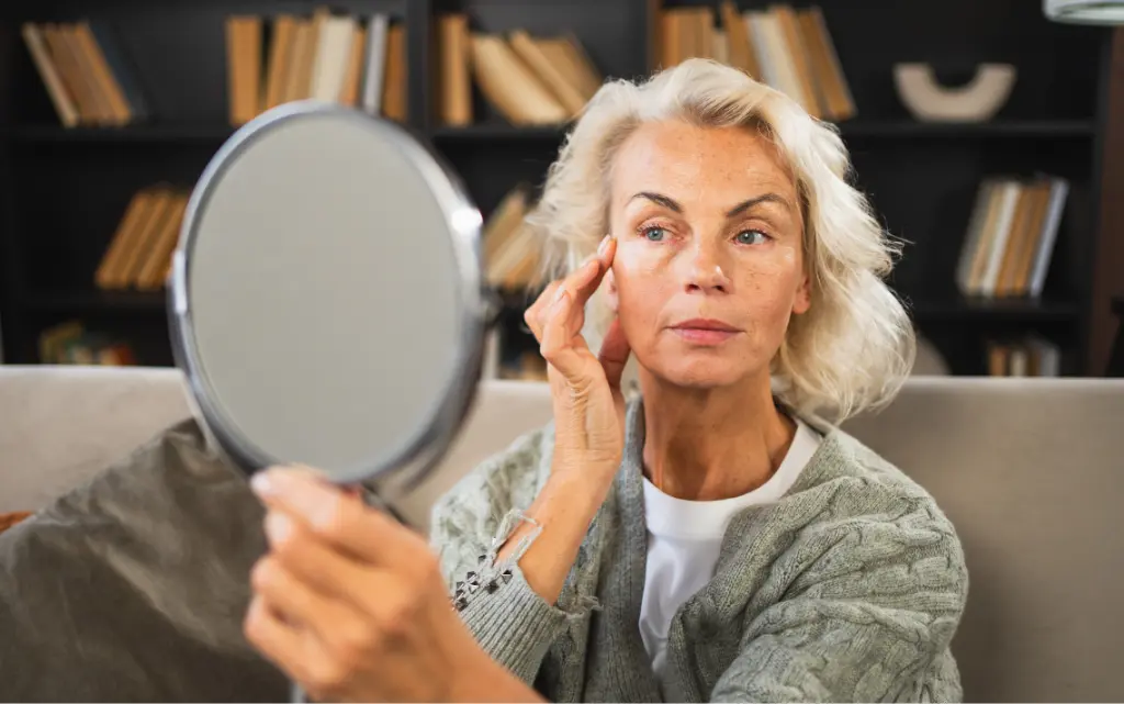 Dojrzała, pomalowana kobieta przygląda się w lusterku w pokoju z książkami