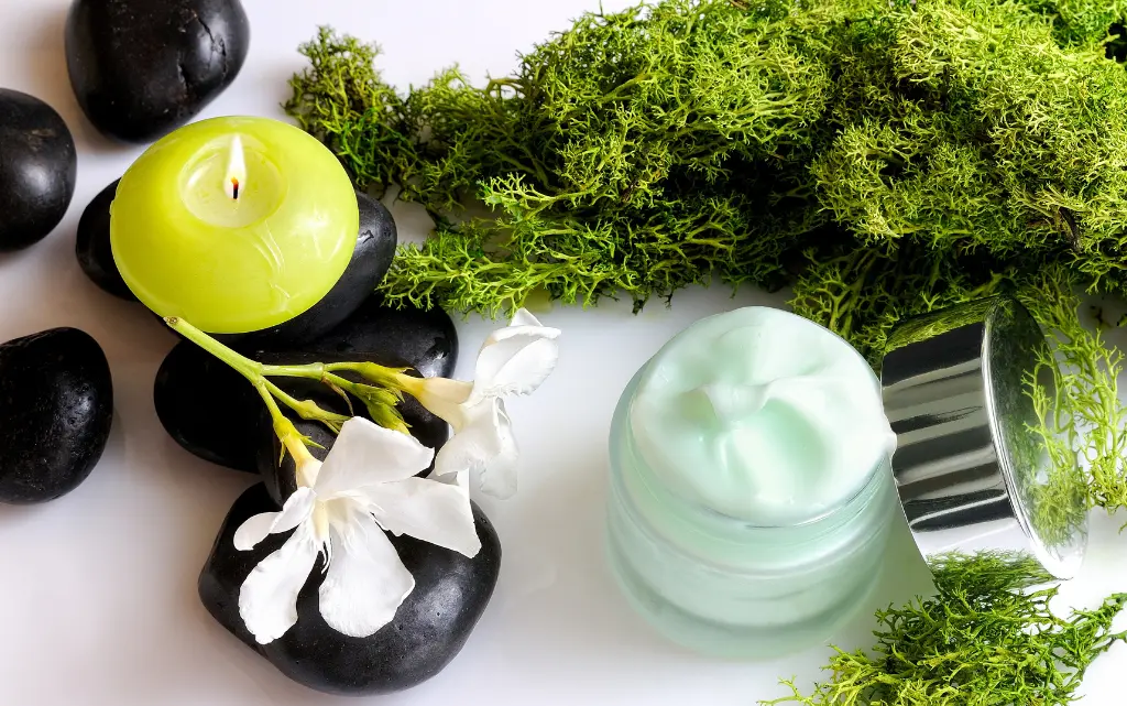 Zielone glony morskie, obok czarne kamienie, żółta świeczka i słoik z zielonym kremem