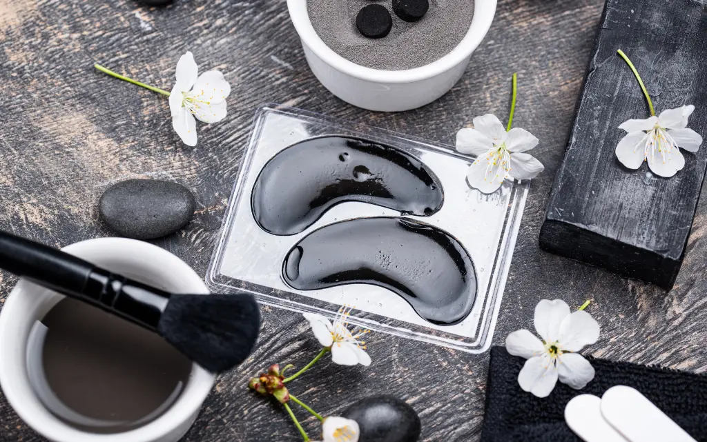 Na blacie płatki pod oczy z węglem aktywnym, czarny pędzel, sproszkowany węgiel w pojemniczku oraz dla dekoracji białe kwiatki wiśni