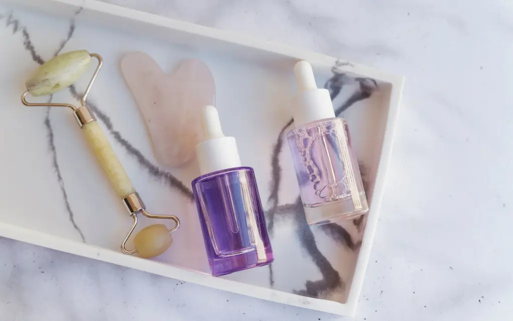 Na marmurowym blacie taca, na niej masażery do twarzy i dwie butelki serum z bakuchiolem