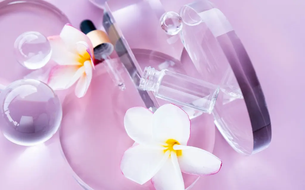 Fioletowo-różowe tłom, na nim białe kwiaty, pusta butelka, pipetka oraz białe kwiaty