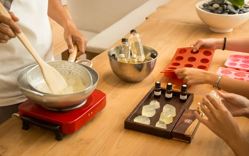 Stół kuchenny, na nim składniki i gliceryna niezbędne do domowej produkcji mydła, widok na kobiece dłonie produkujące mydło