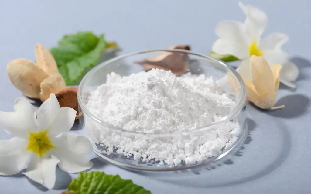 Wieczko z proszkiem allantoiny, obok zielone liście i białe kwiaty