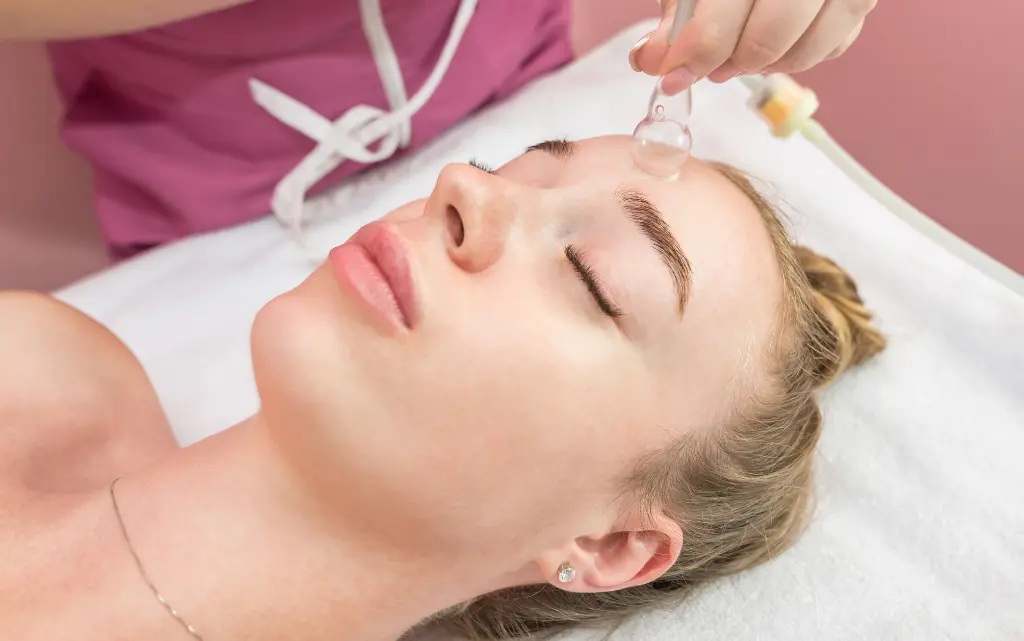 Kobieta u kosmetyczki poddaje się zabiegowi masażu chińską bańką po twarzy