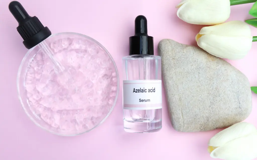 Butelka z kwasem azelainowym, obok pipetka ze szkiełkiem laboratoryjnym, szary kamień oraz białe tulipany