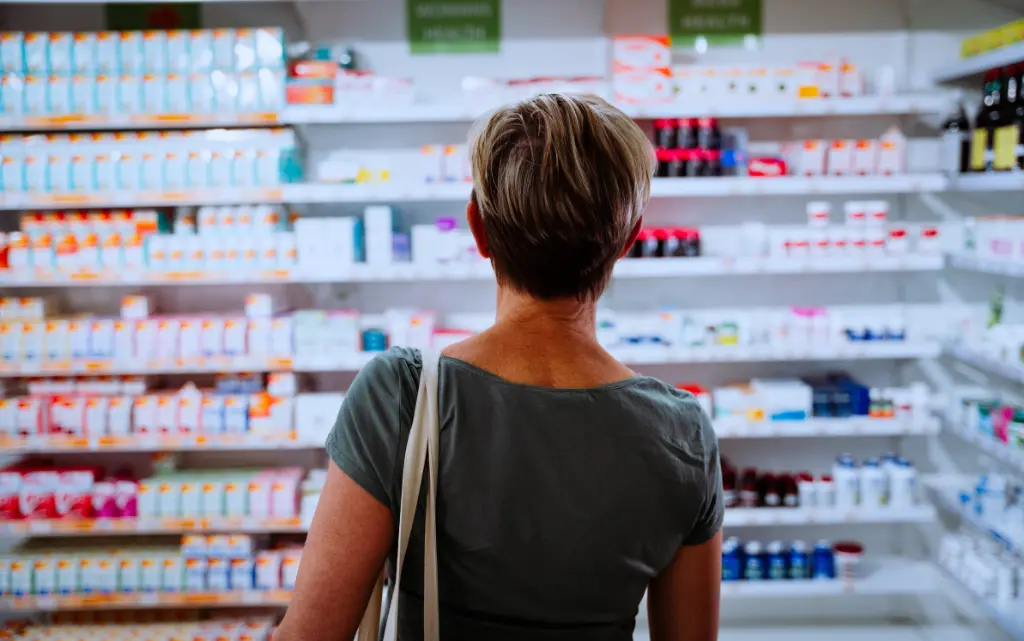 Kobieta w średnim wieku stoi przed półkami w drogerii i zastanawia się, jaki krem na zmarszczki wokół ust wybrać