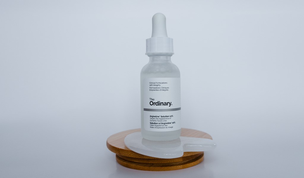 The Ordinary Argireline Solution 10% – Serum z 10% kompleksem peptydów Argireline na drewnianej podstawce i quasha - zdjęcie.