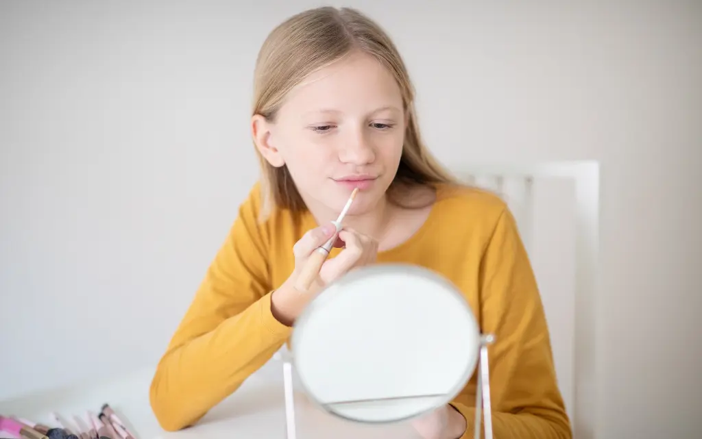 Nastolatka maluje usta błyszczykiem przed lusterkiem