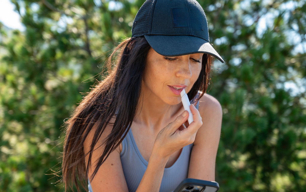 Kobieta na dworze w kaszkietówce nakłada pomadkę ochronną na spierzchnięte usta