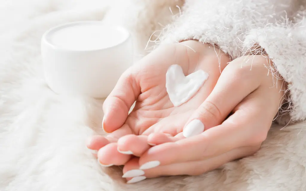 Złożone kobiece dłonie, w środku serduszko z kremu nawilżającego do twarzy