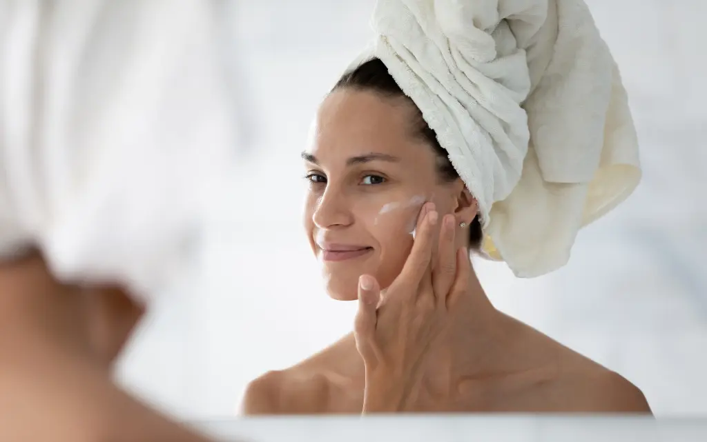 Młoda kobieta przed lustrem nakłada krem nawilżający na twarz