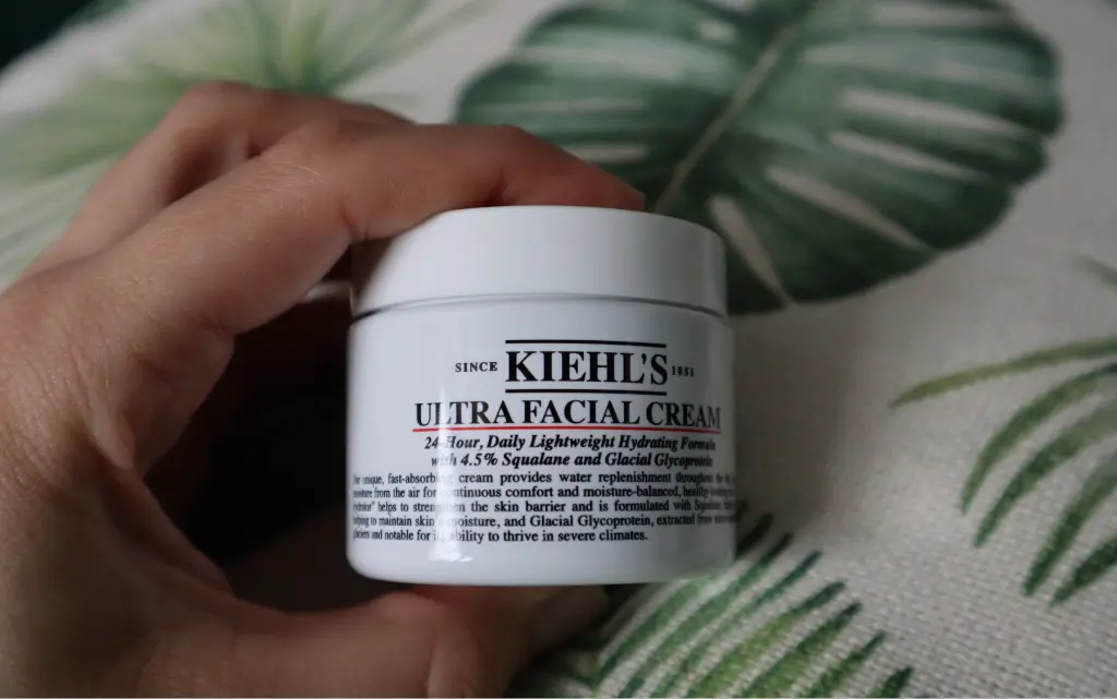 Krem nawilżający do twarzy Kiehl’s Ultra Facial Cream na tle beżowo-zielonej poduszki