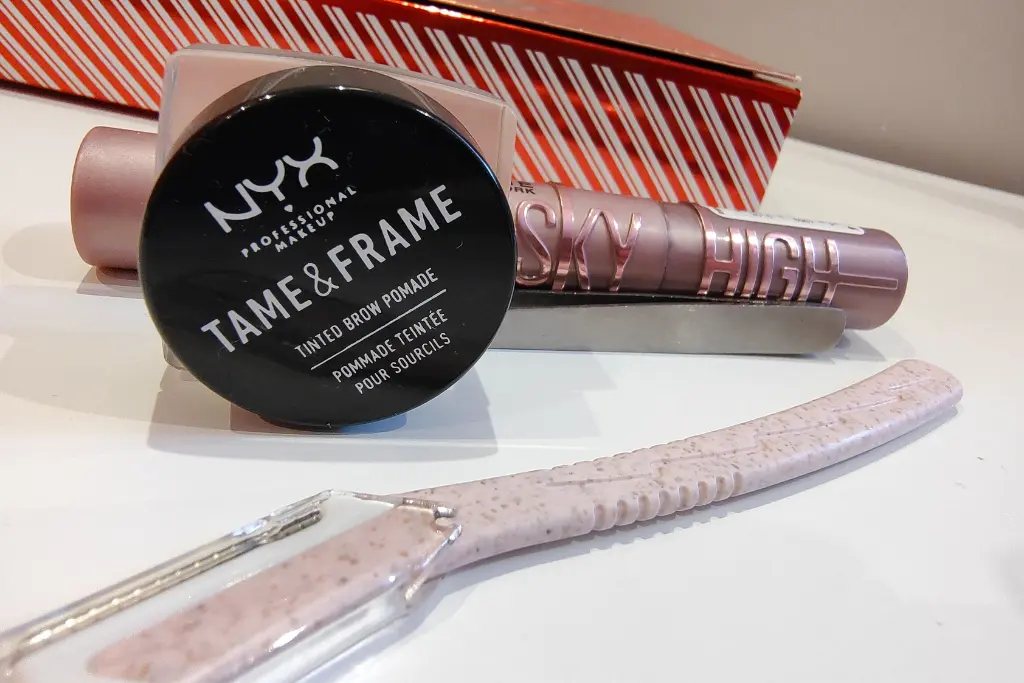Pomada do brwi NYX, obok tusz Maybelline Sky Hihgh oraz nożyk do brwi