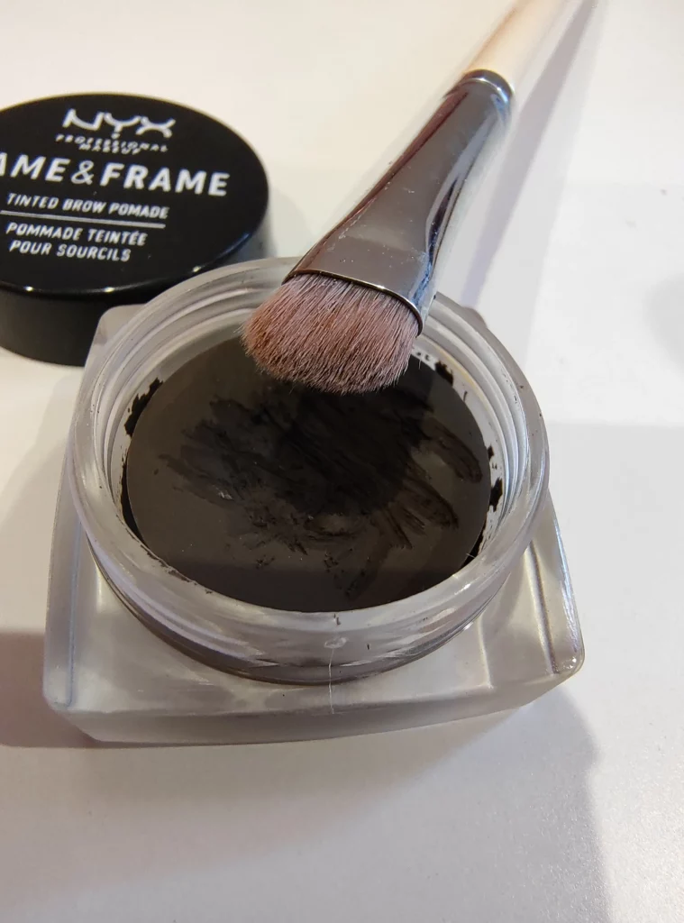 Pędzelek do malikażu na tle opakowania pomady do brwi NYX