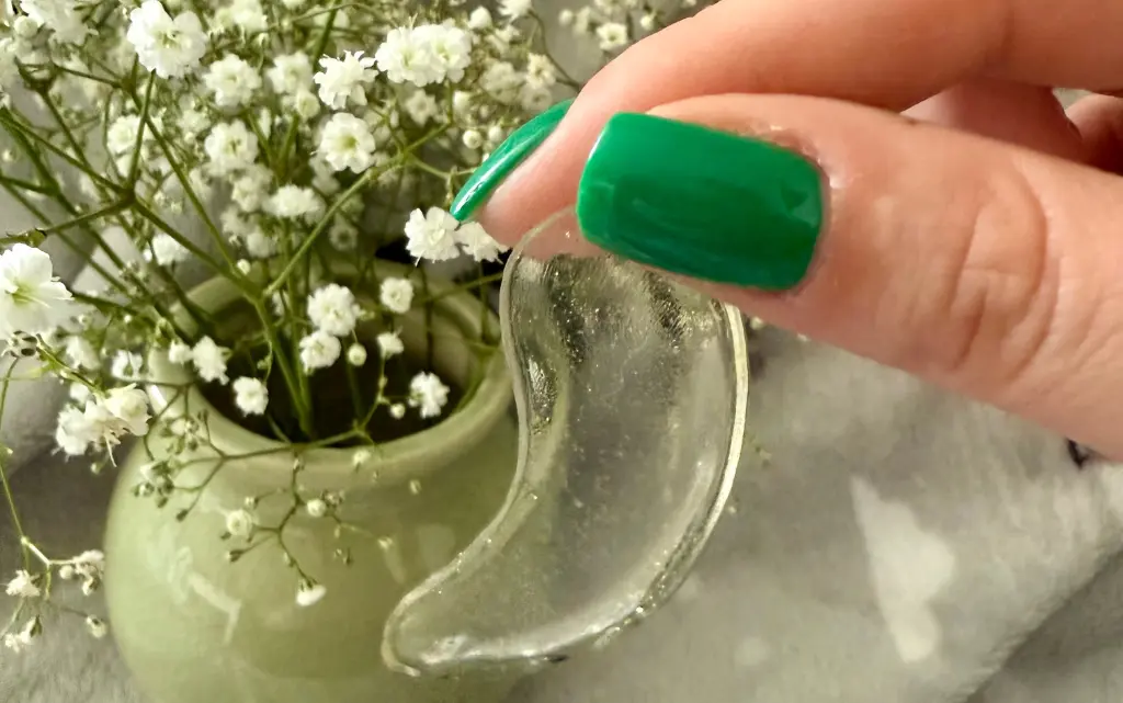 Hydrożelowe płatki pod oczy kompres rozświetlający Eveline trzymane przez kobietę z zielonym manicure