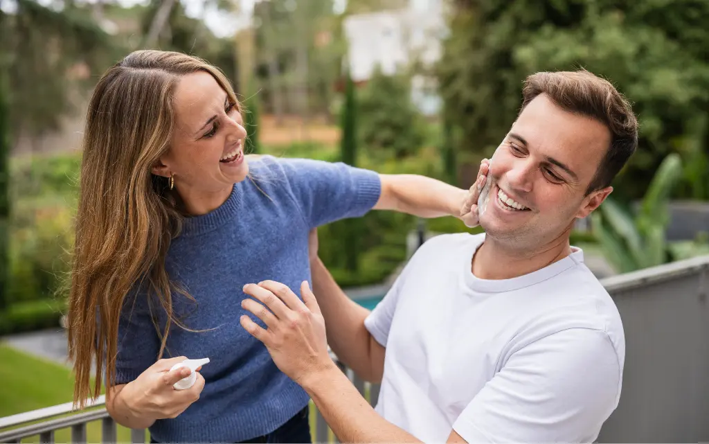 Uśmiechnięta para w parku, kobieta nakłada krem z SPF na twarz mężczyzny
