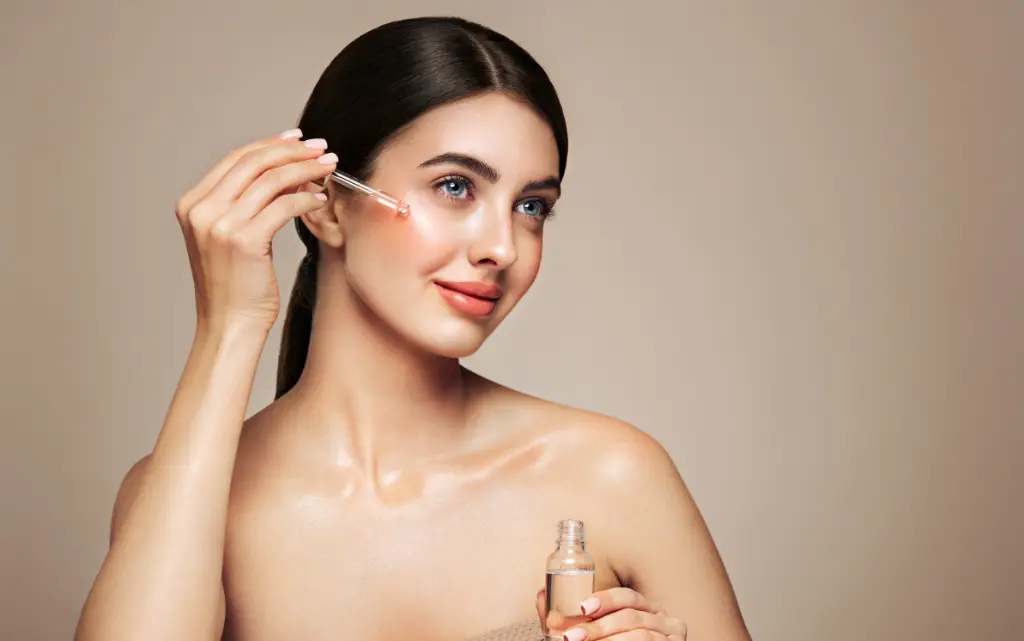 Młoda kobieta aplikuje na twarz w makijażu glow up krople nawilżające