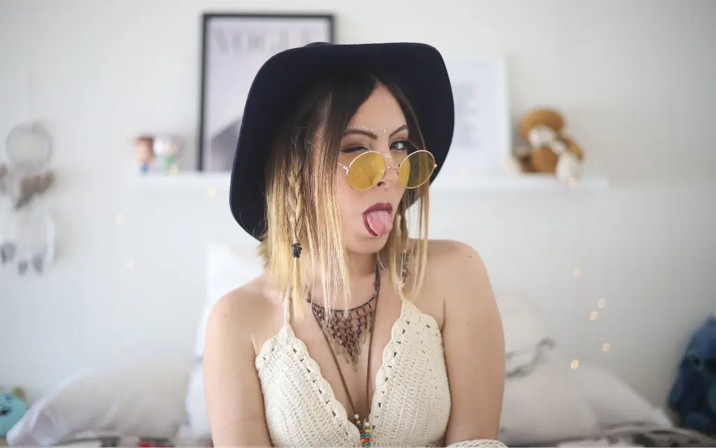 Młoda kobieta w festiwalowym ubraniu i makijażu w pokoju pokazuje język