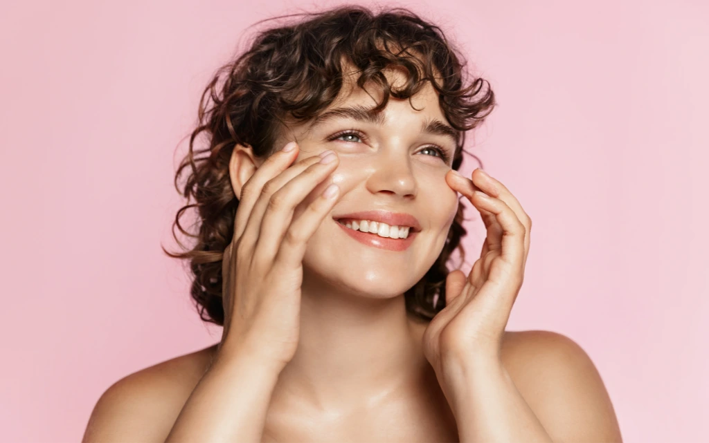 Uśmiechnięta młoda kobieta dotyka rękami swojej zdrowej, normalnej cery