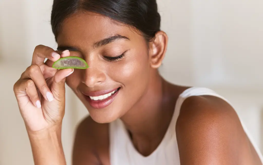 Uśmiechnięta kobieta z zamkniętymi oczami trzyma kawałek aloesu