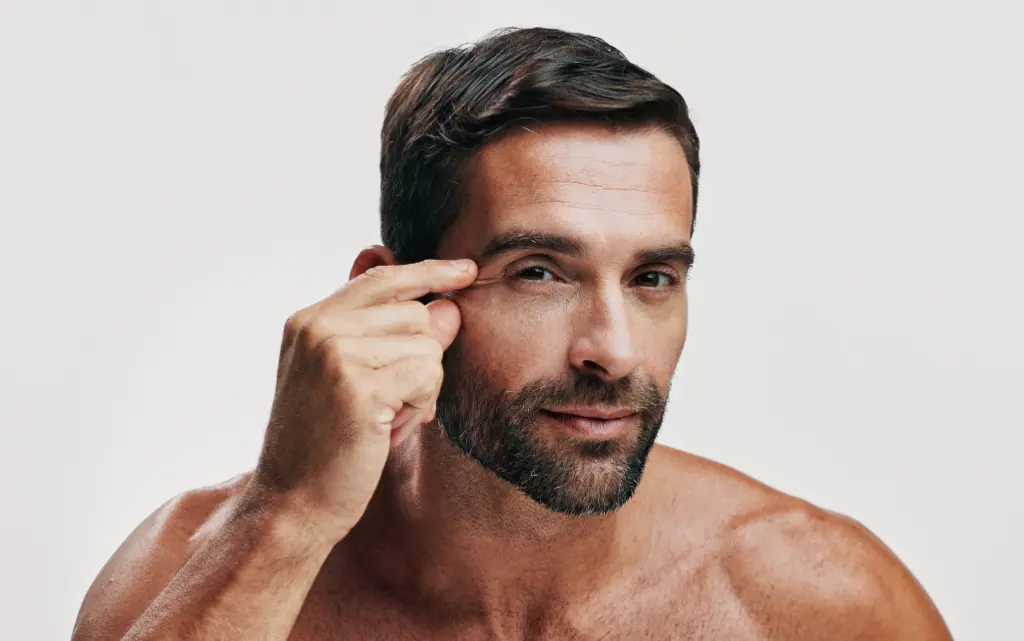 Dojrzały mężczyzna ściska na twarzy skórę i uwydatnia zmarszczki mimiczne