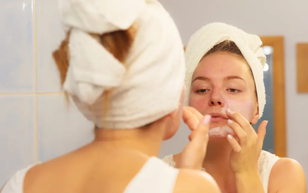 Młoda kobieta przed lustrem nakłada na twarz krem nawilżający do cery odwodnionej