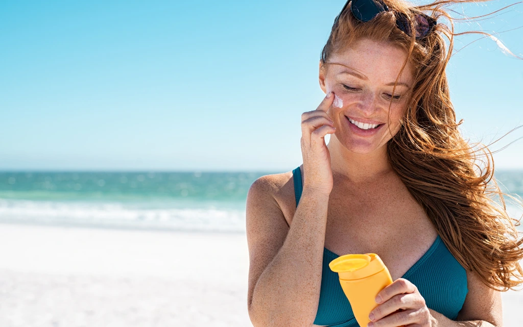 Kobieta na twarzy w lecie nakłada krem z filtrem na twarz