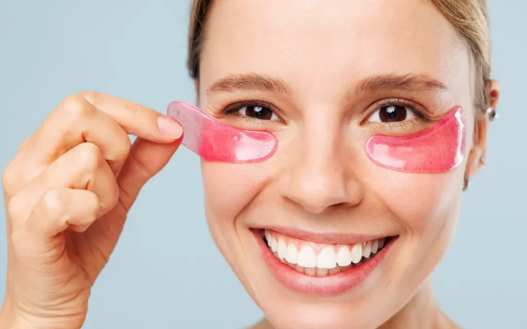 Młoda kobieta nakłada płatki hydrożelowe pod oczy by zlikwidować cienie pod oczami