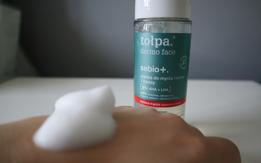 Na drugi tle wyraźne opakowanie pianki Tołpa Dermo Face Sebio+, na pierwszym planie rozmazana pianka na dłoni