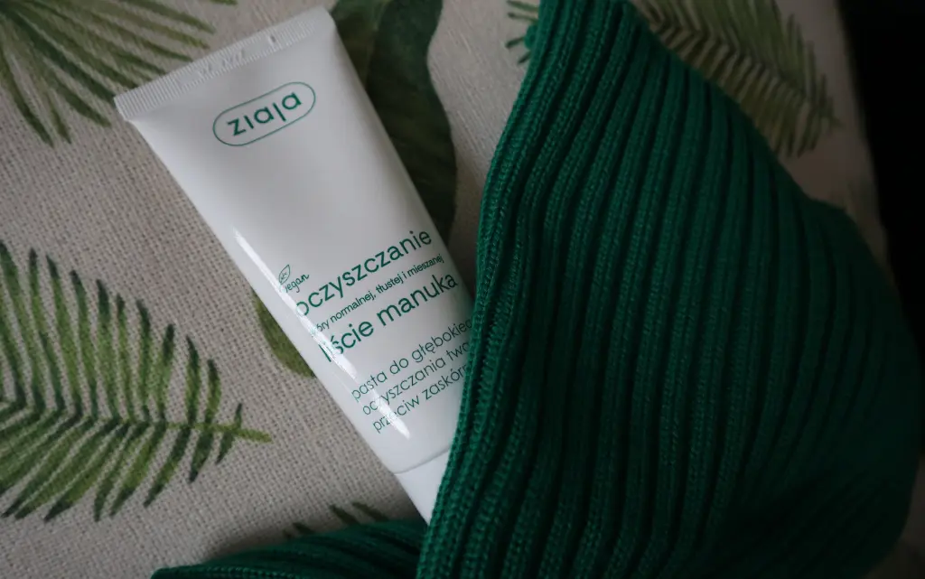 Pasta do zaskórników Ziaja liście manuka na tle beżowej poduszki i obok zielonego szalika