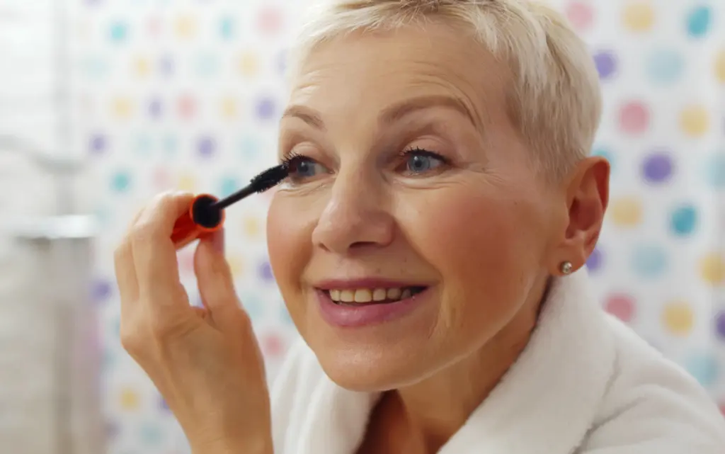 Uśmiechnięta starsza pani robi makijaż oka przy opadającej powiece
