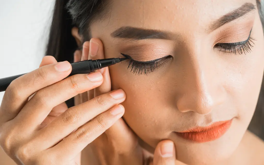 Młoda kobieta robi kreski eyelinerem w makijażu opadającej powieki