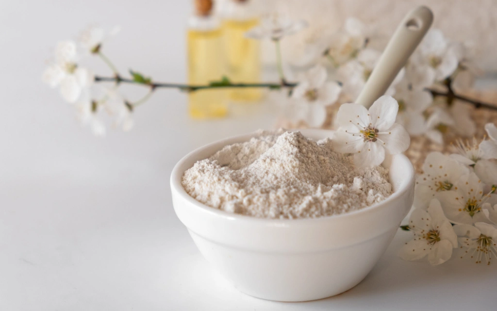 Sproszkowana glinka bentonitowa w porcelanowej miseczce, w tle białe kwiaty