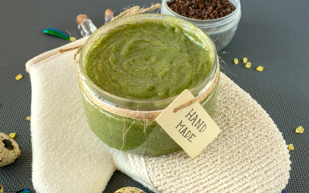 Domowa maseczka do twarzy z zielonej herbaty w słoiczku, w tle rękawica do masażu twarzy