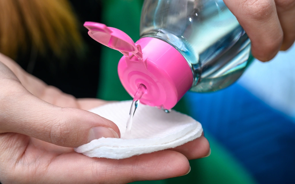 Kobiece dłonie trzymają tonik do twarzy i nalewają trochę kosmetyku na wacik