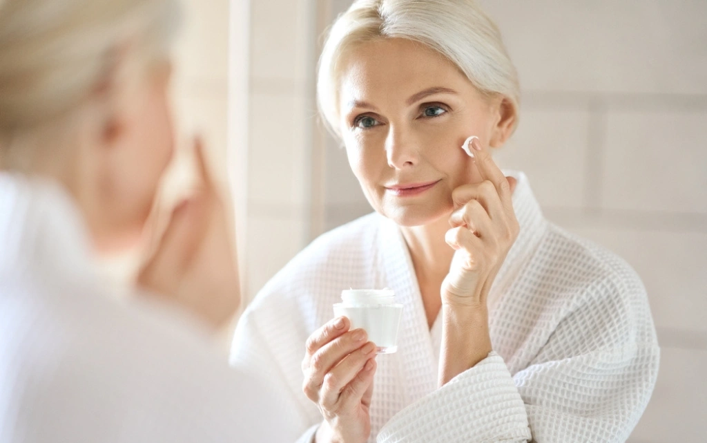 Dojrzała kobieta nakłada krem na przesuszoną skórę twarzy
