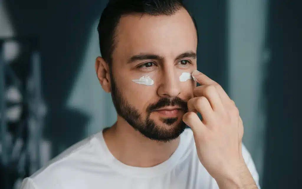 Mężczyzna nakładający krem na twarz i w okolice oczu