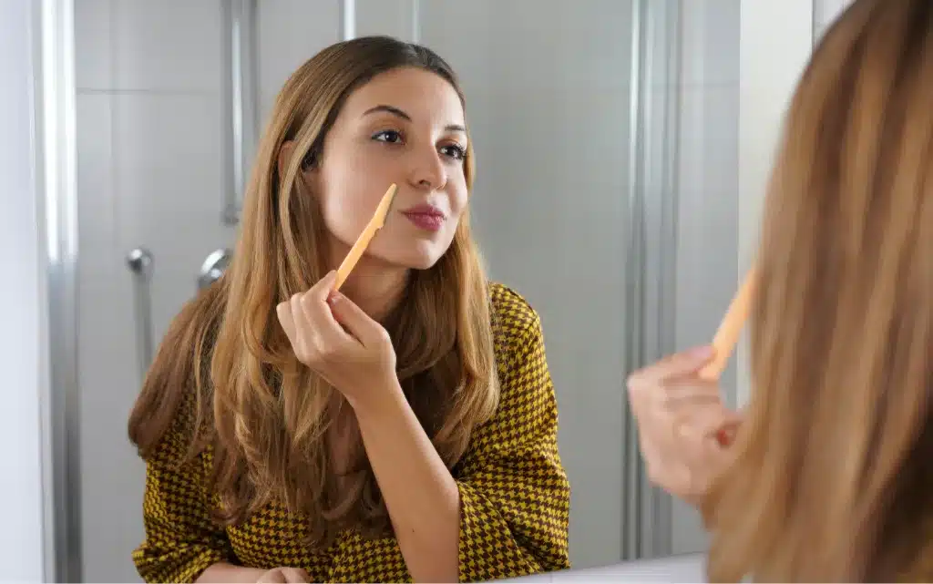 Młoda kobieta używa nożyka do golenia twarzy podczas dermaplaningu