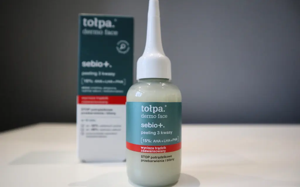 Tołpa Sebio+ Peeling 3 Kwasy na tle szarej ściany, wyjęty z papierowego opakowania