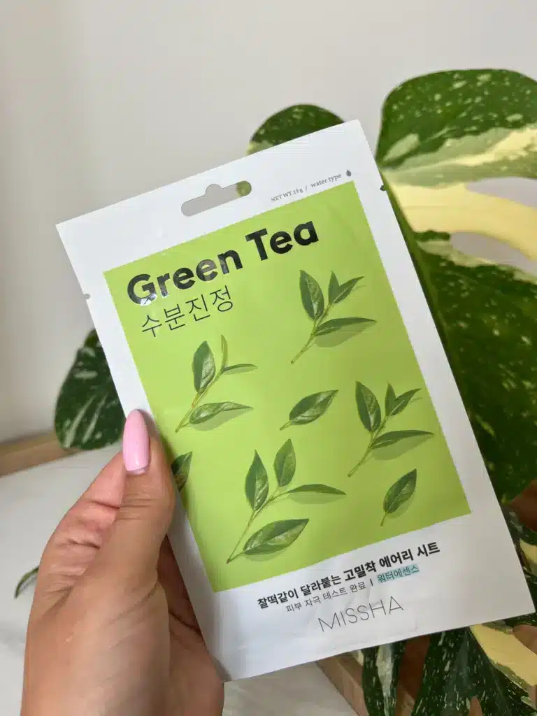 Kobieca dłoń trzyma maseczkę w płachcie Missha Green Tea