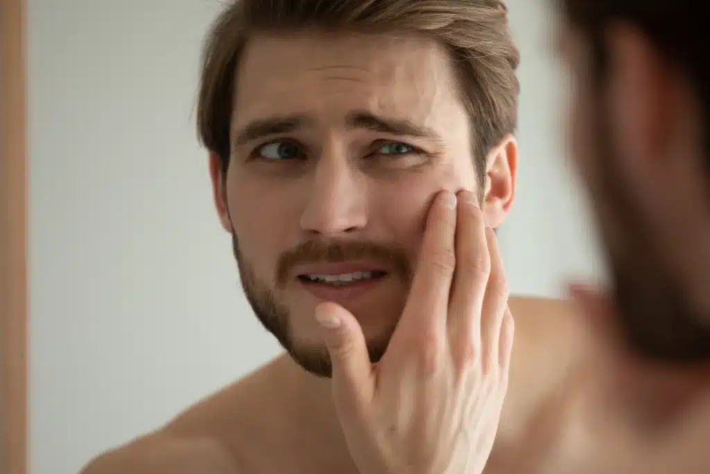 Zaniepokojony mężczyzna ocenia stan swojej cery przed lustrem
