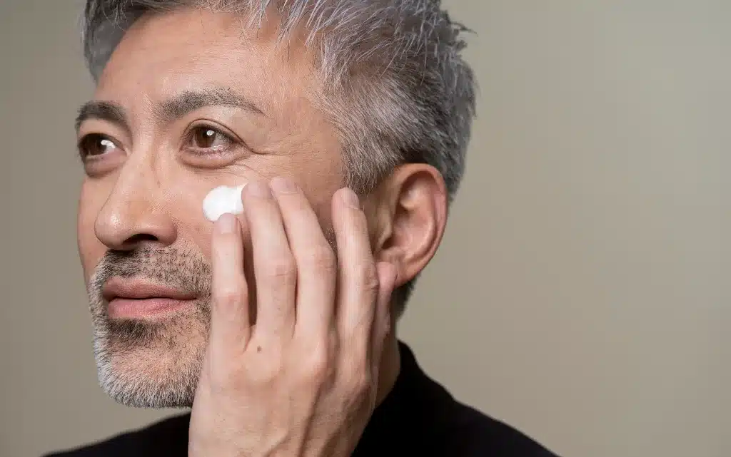 Mężczyzna w średnim wieku nakłada na twarz krem nawilżający