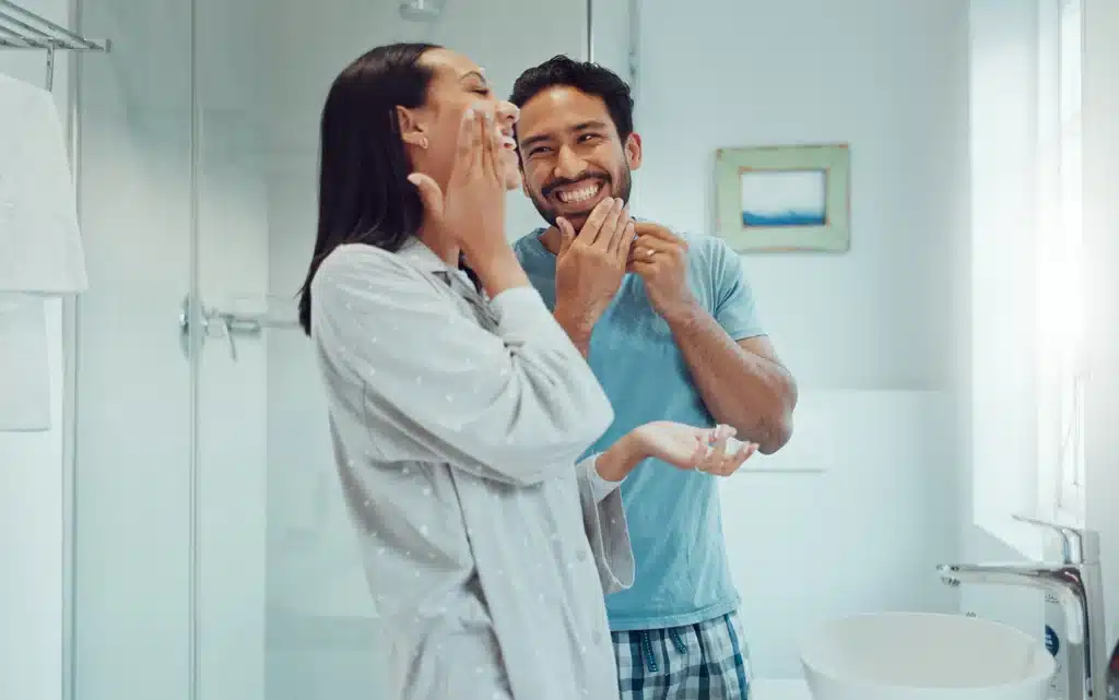 Uśmiechnięta para w łazience nakłada krem na twarz na początek dnia